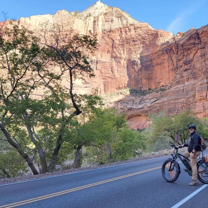Mann auf Fahrrad steht auf Straße mit großen roten Felsen im Hintergrund
