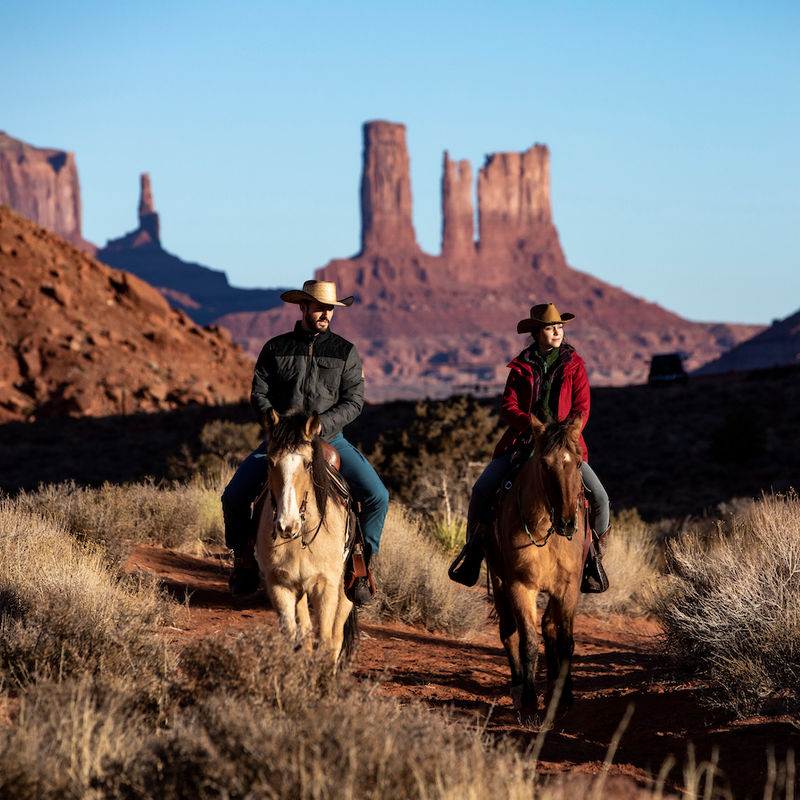 Pärchen reitet auf Pferden durch rote Felslandschaft in Utah