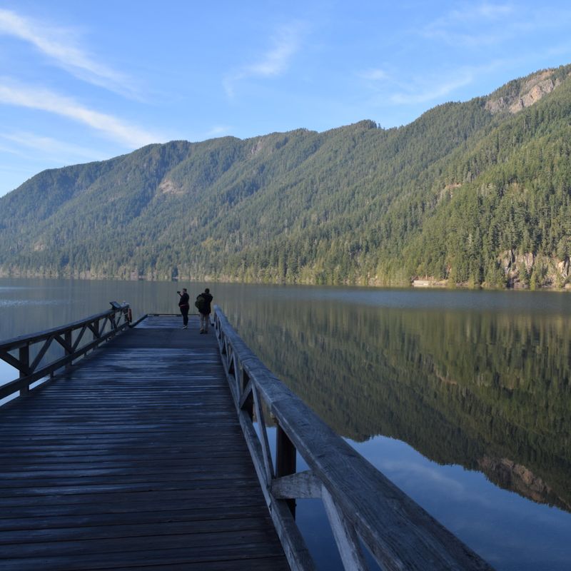 Een houten steiger die uitkijkt over een helder meer met beboste bergen op de achtergrond