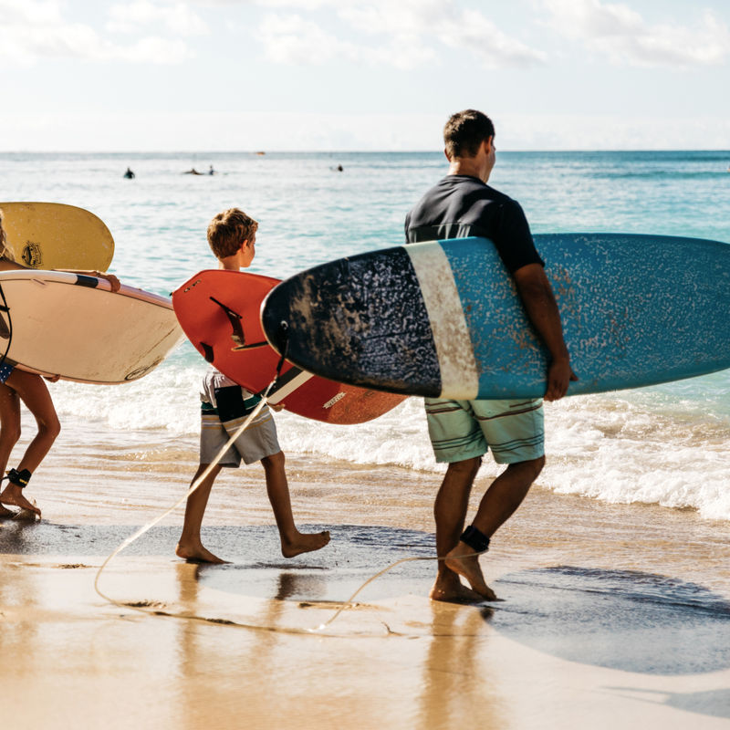 Een gezin van vier staat op het strand in Hawaï, met ieder een surfplank in de hand