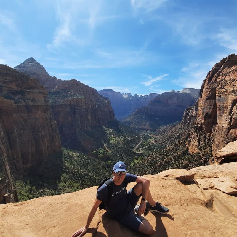 Alain zittend op de grond met uitzicht op Zion National Park in Utah