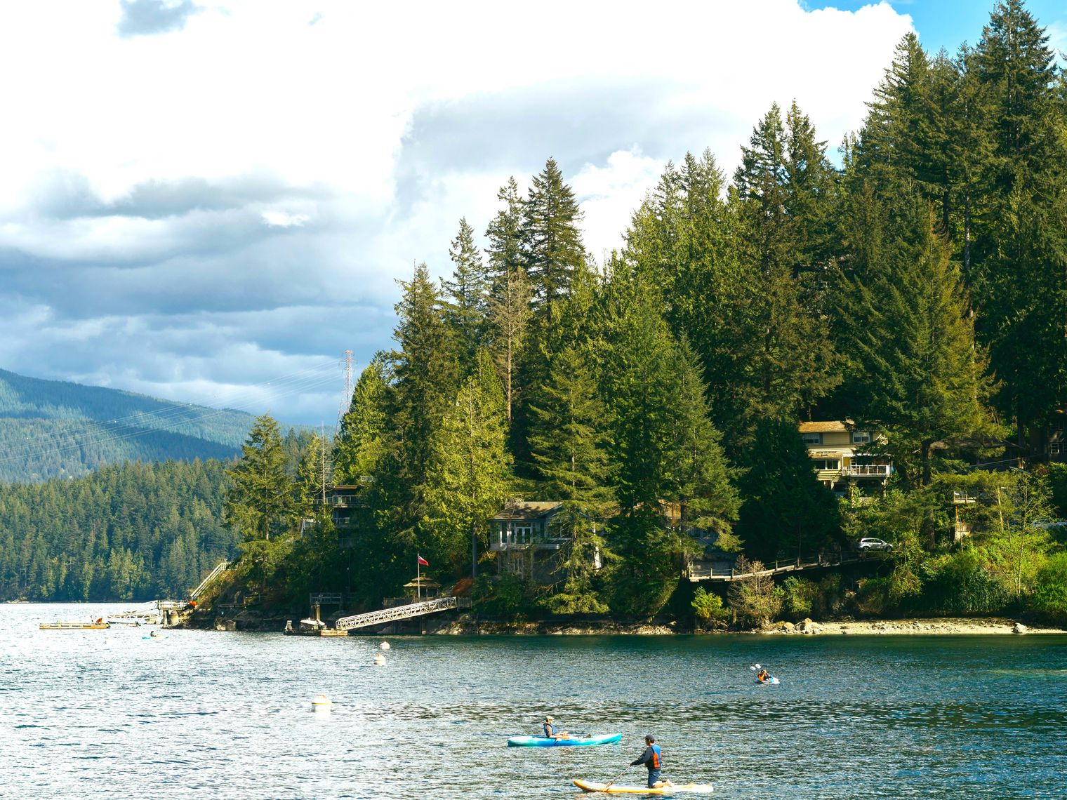 Ein ruhiger See mit bewaldetem Ufer und Kayak-Fahrern in Vancouver, Kanada