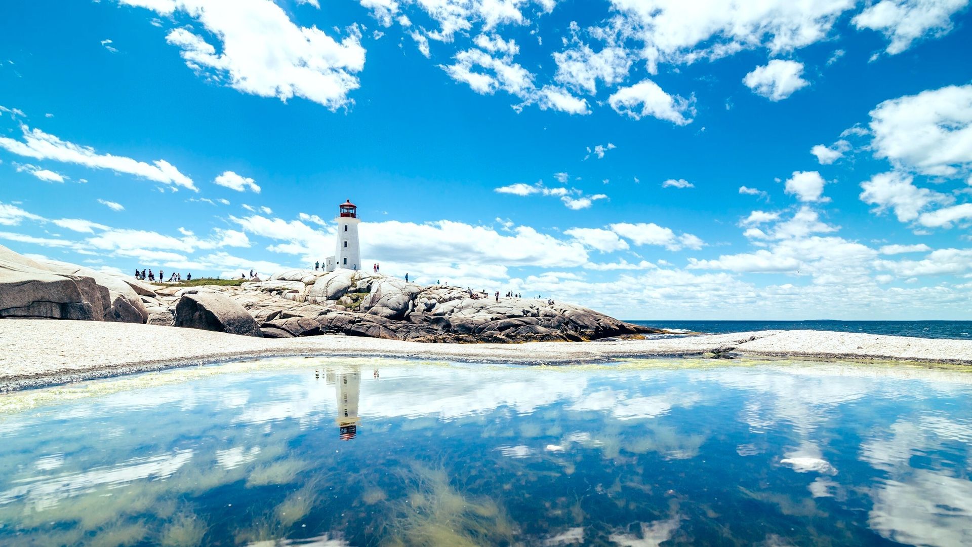 De vuurtoren van Peggy's Cove weerspiegeld in een getijdenpoel aan de rotsachtige kust van Nova Scotia