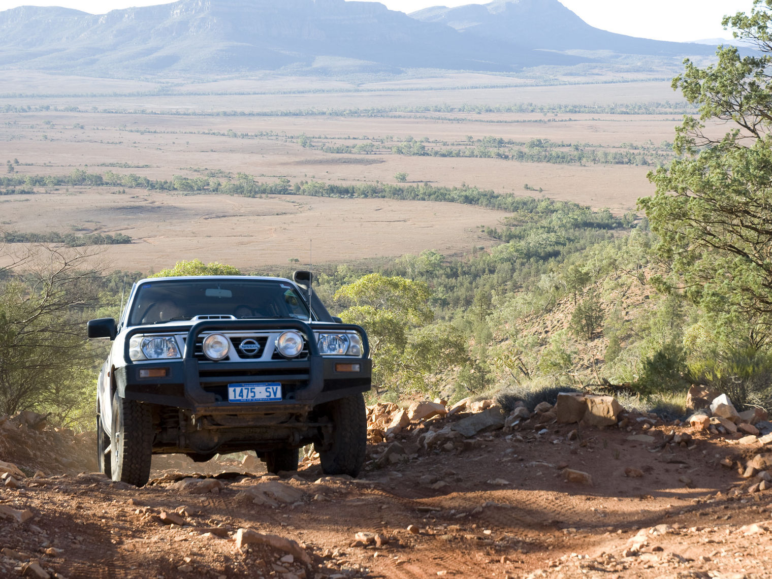 4WD car driving on an uphill dirt road with fields and mountains in the background