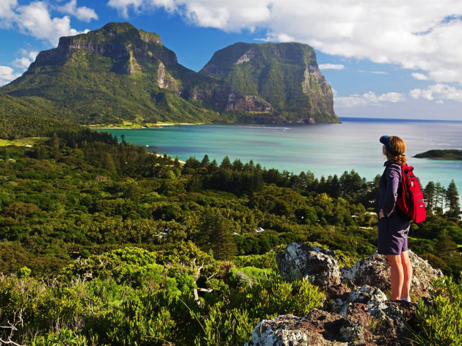 Eine wandernde Frau blickt auf das Meer und die Berge im Hintergrund
