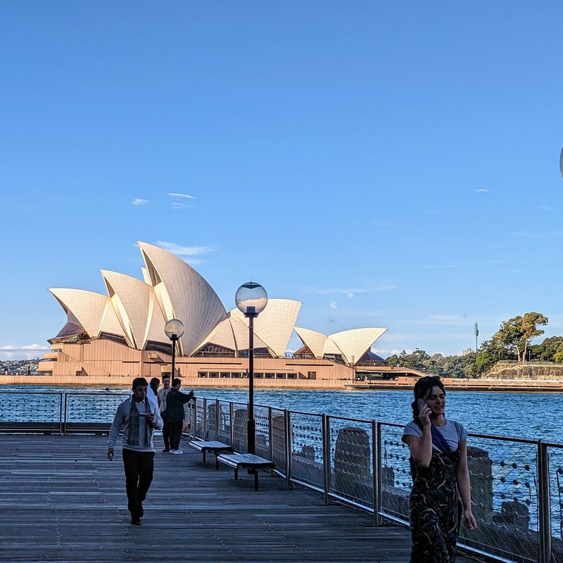 Blick auf das Opernhaus von Sydney von einem Steg aus, auf dem Menschen spazieren gehen