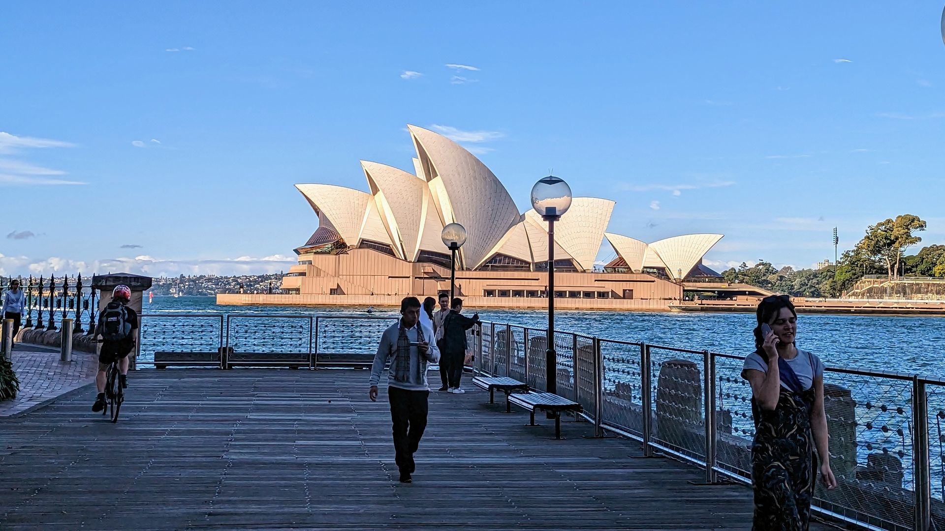 Blick auf das Opernhaus von Sydney von einem Steg aus, auf dem Menschen spazieren gehen