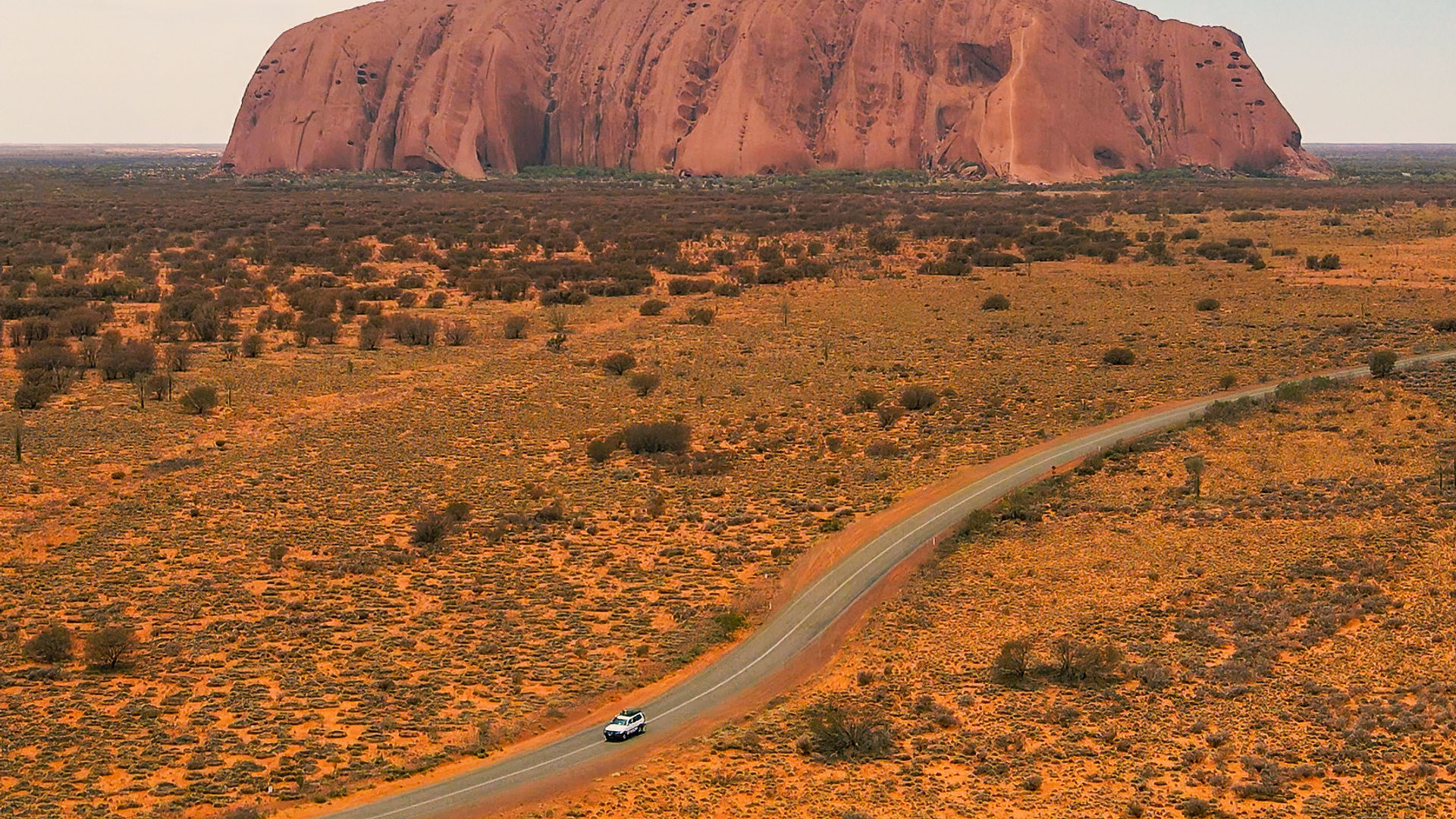 A car driving down a road with Uluru in the background