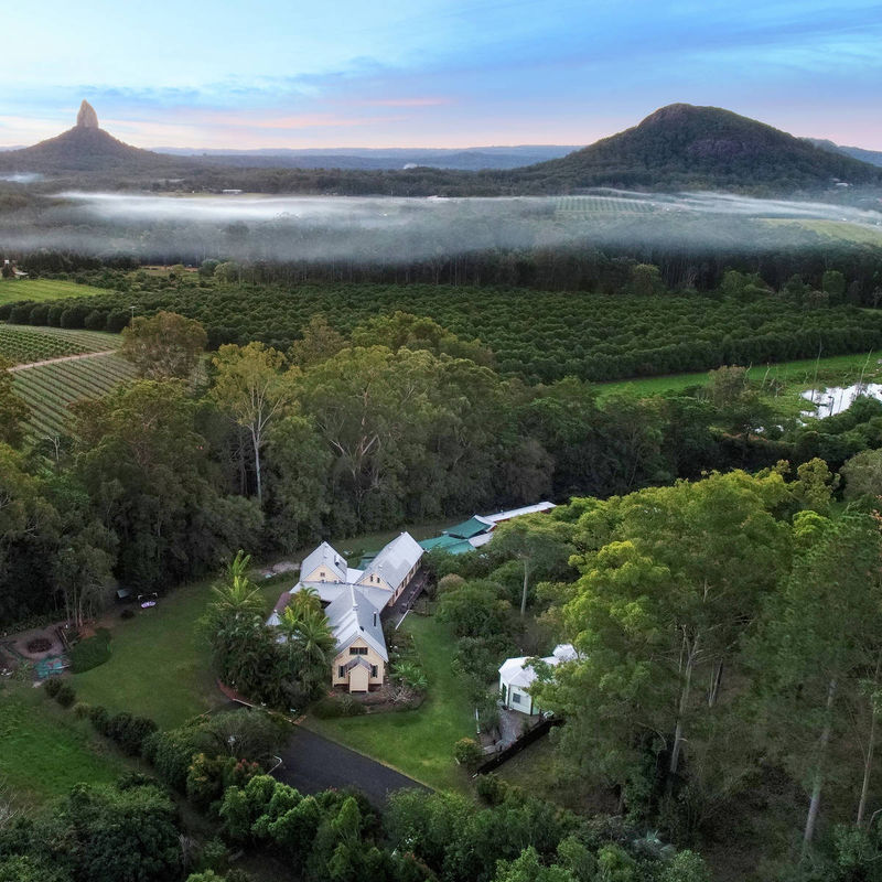 A lodge sits surrounded by greenery with Australia's Glasshouse Mountains in the background