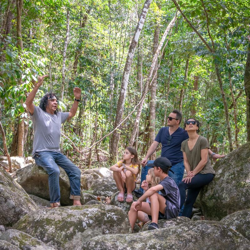 Local guide sits on rocks in the Queensland rainforest with a family while telling them about their surroundings