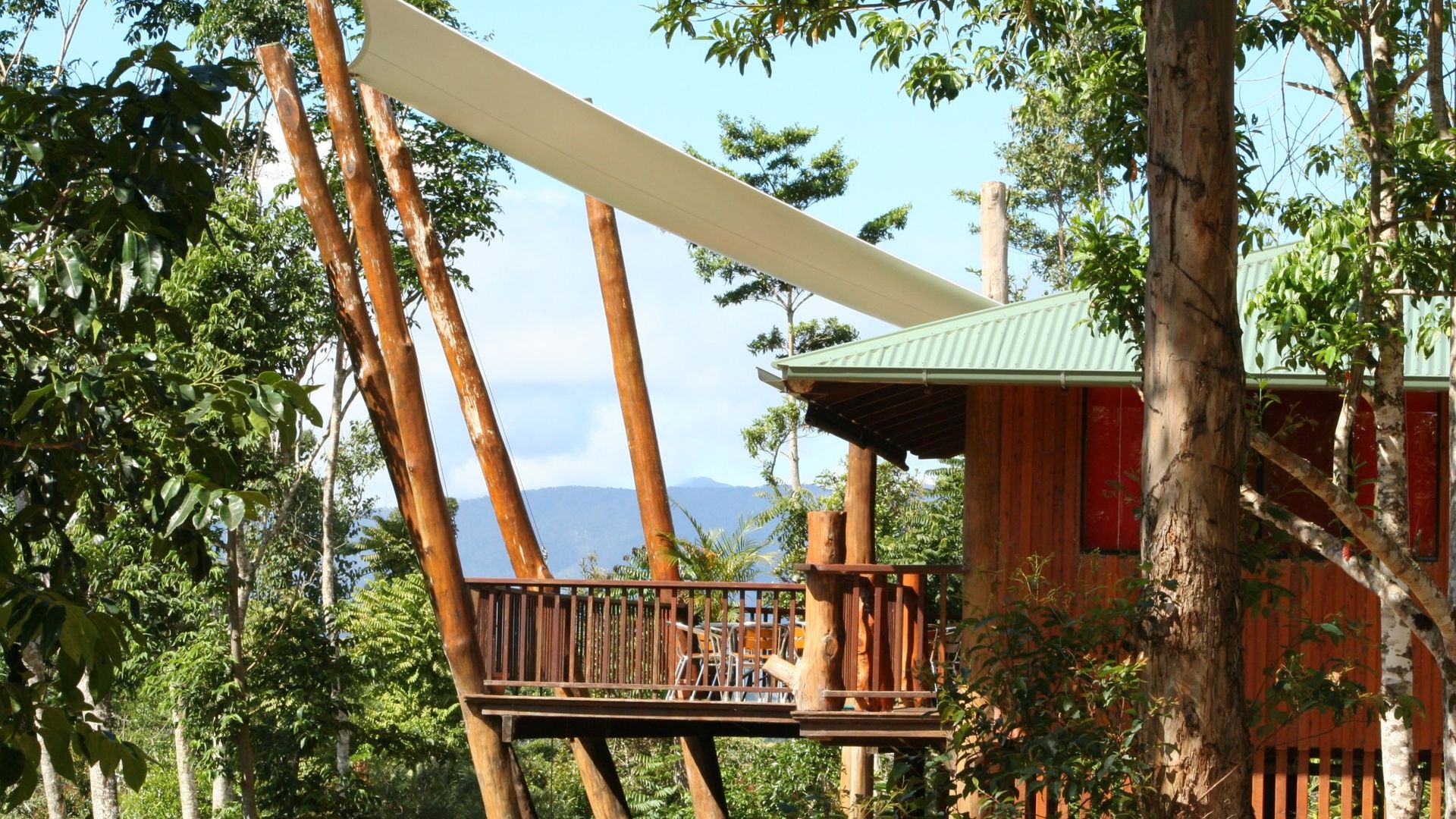Erhöhtes Baumhaus mit umlaufender Terrasse und Sonnensegel, eingebettet zwischen üppigen Regenwäldern mit Bergblick, einzigartige Öko-Unterkunft in Australien