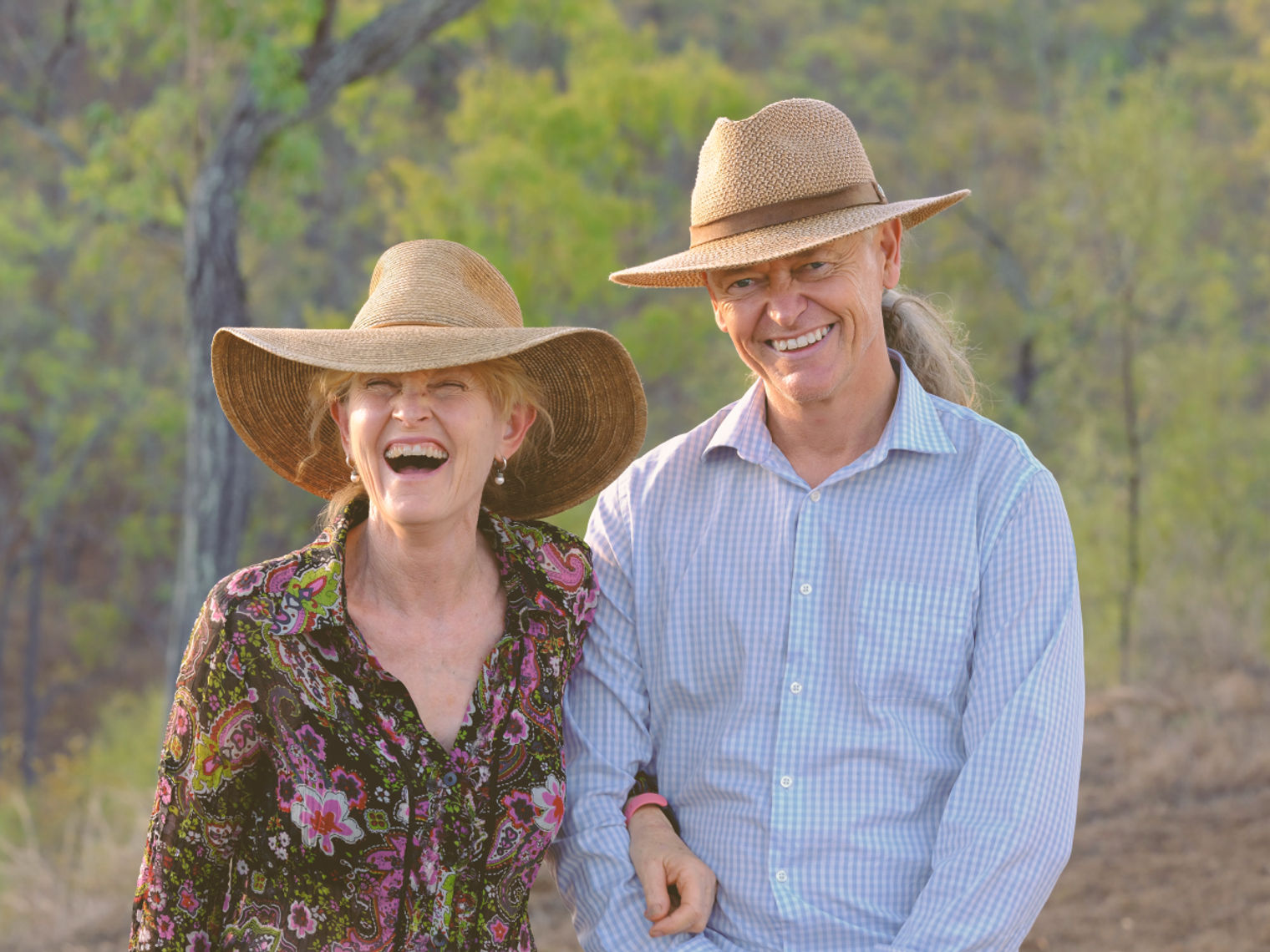 Smiling couple wearing wide-brimmed hats in the Australian outback of Queensland, local farmstay hosts welcoming guests in a rural bush setting