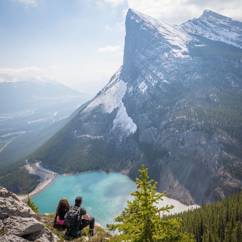 Ein Paar sitzt an einem Aussichtspunkt in Canmore mit Blick auf einen See und einen schroffen Berggipfel