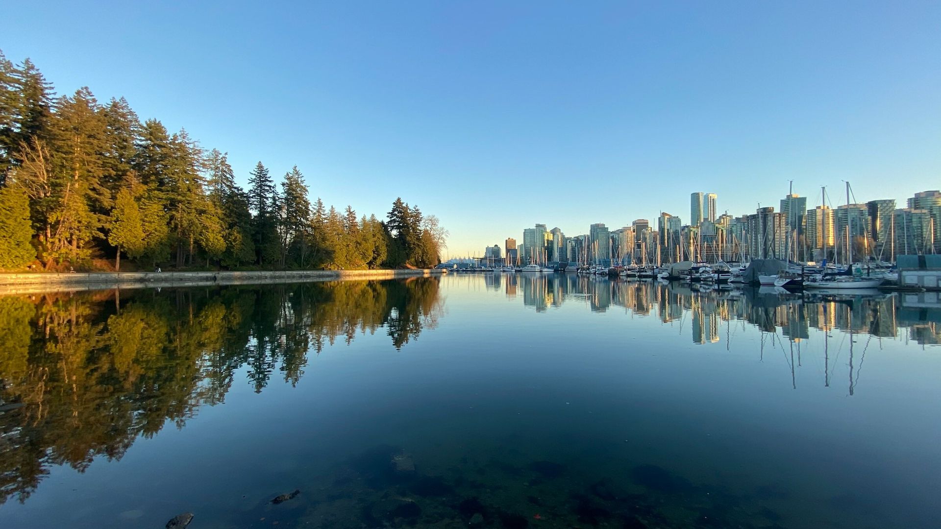 Vancouver skyline reflected in calm water at sunset, seen from the shoreline near Stanley Park