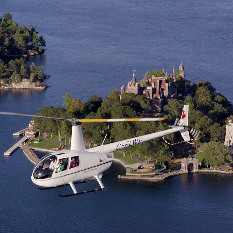 View of a white helicopter flying with passengers of an island with a castle in the Thousand Island, Eastern Canada