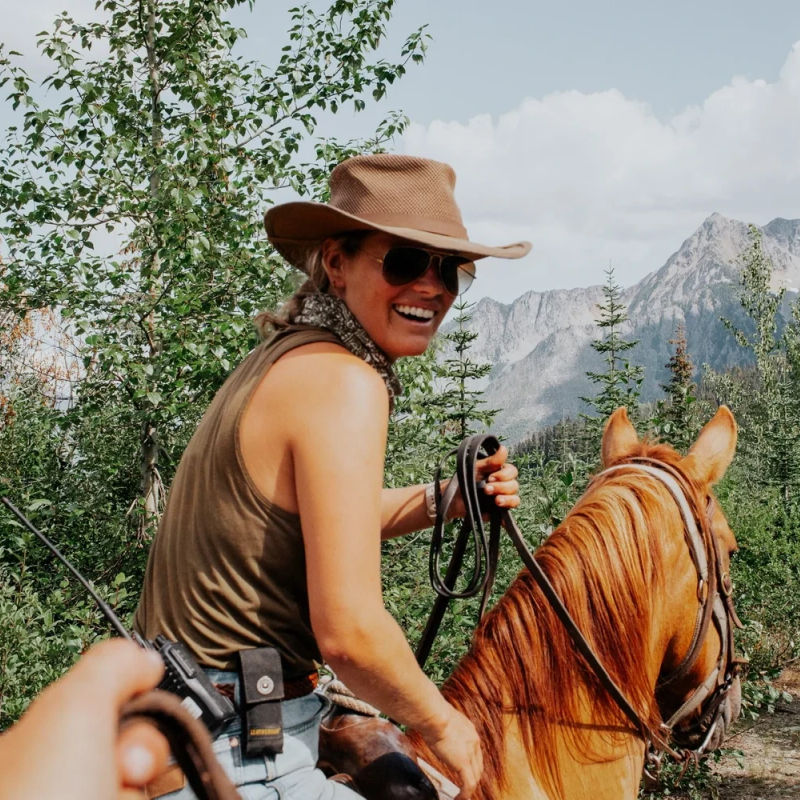 A local guide rides a horse and smiles back at the camera with mountains and trees in the background