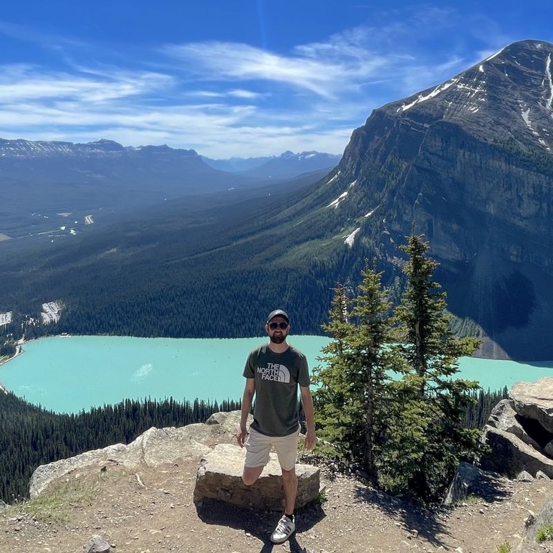 Little America specialist Luke stands in front of Lake Louise in Banff, with trees and mountains in the background