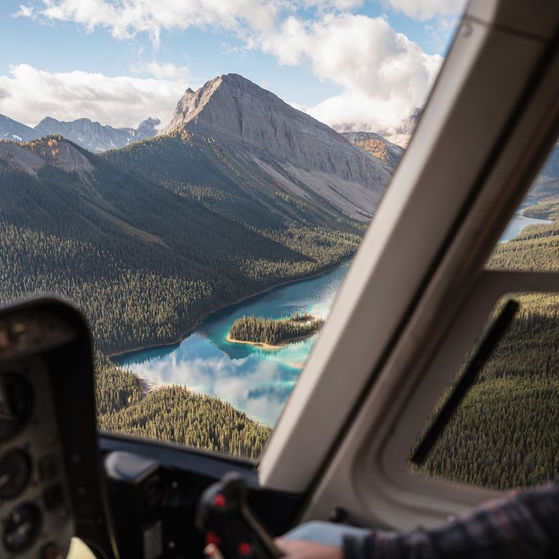 A pilot's view out the helicopter window of the Canadian Rockies with turquoise lakes and forested mountainsides