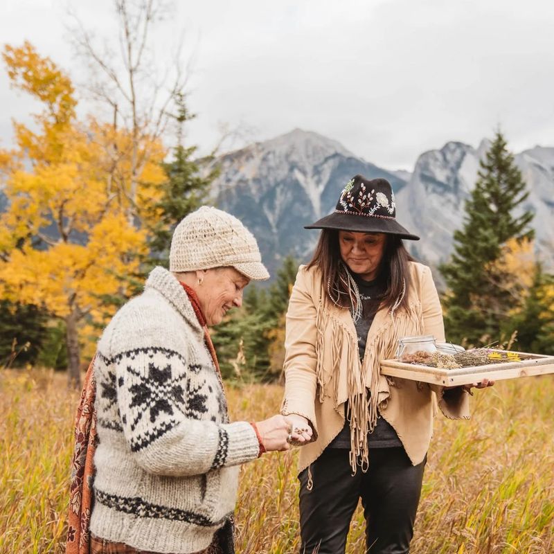 Indigenous female guide shows a woman medicinal herbs in a meadow.