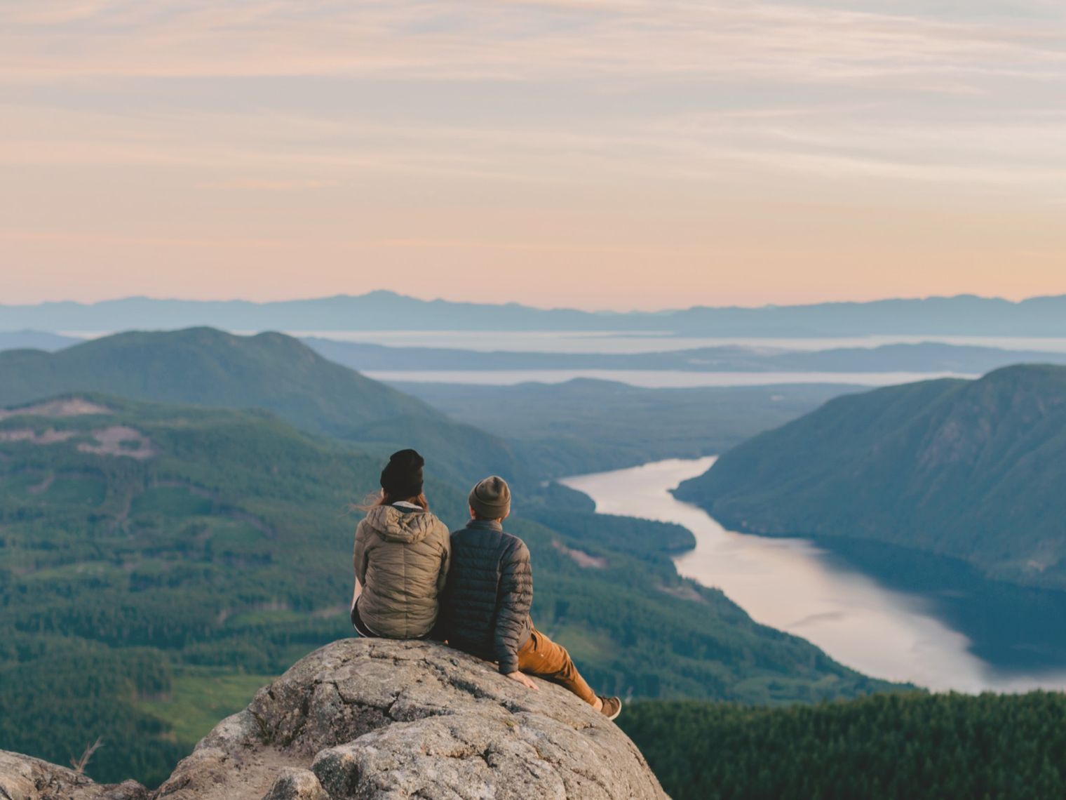 A couple sitting on a rock looking out towards the mountains and lakes, Sunshine Coast
