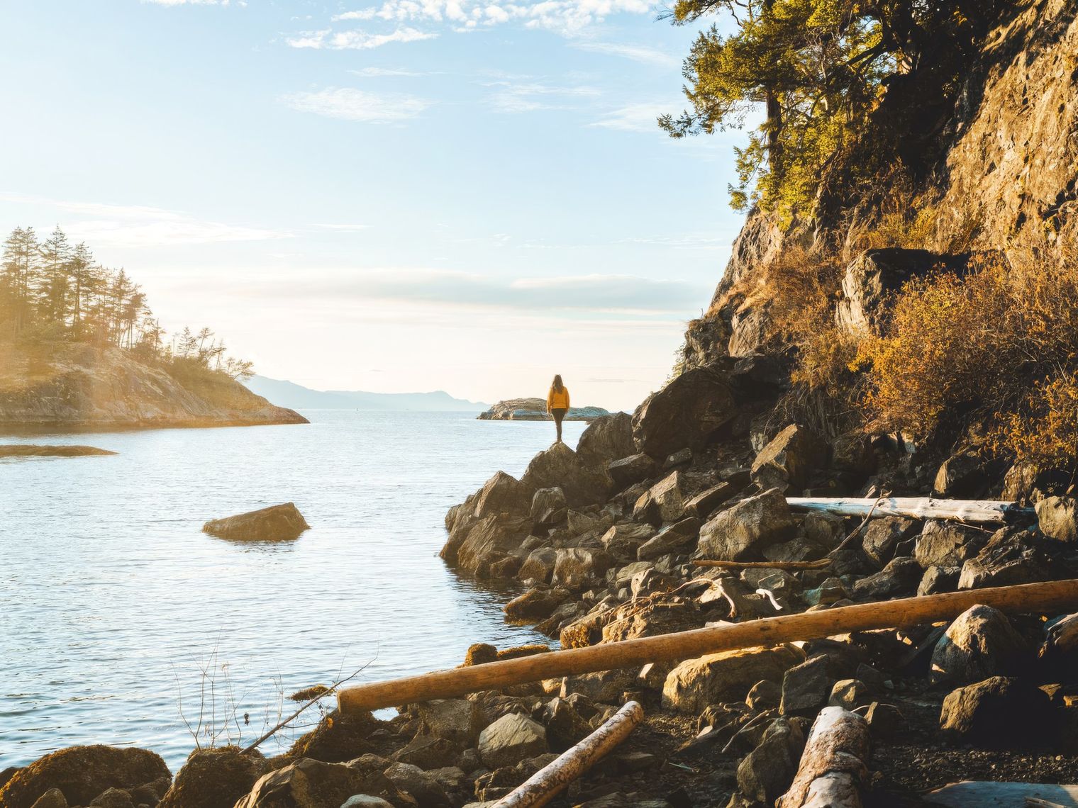 A woman standing at the edge of a rocky shoreline looking out at the view in Sunshine Coast