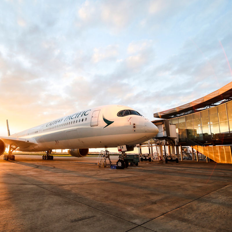 A Cathay Pacific Airbus at the airport with a sunset in the background.