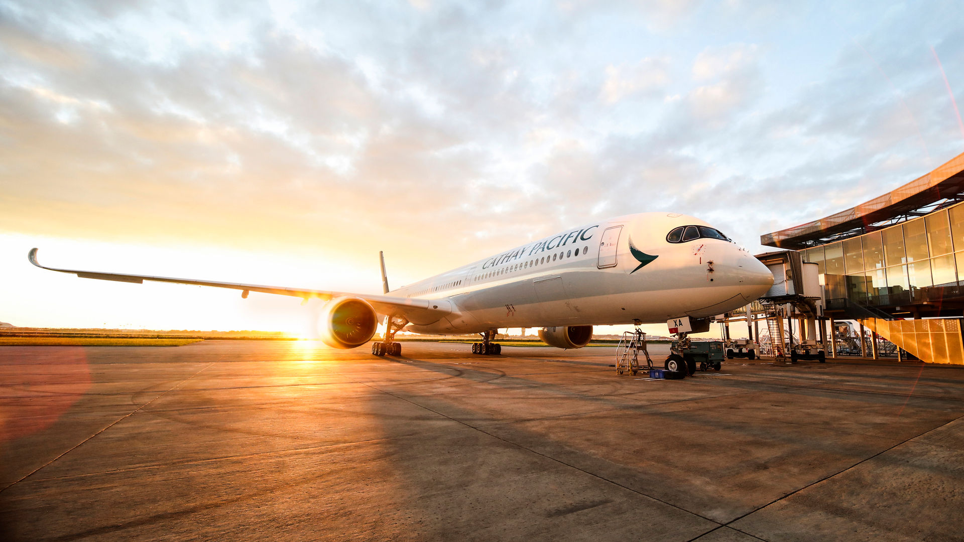 A Cathay Pacific Airbus at the airport with a sunset in the background.