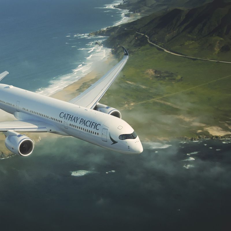 A Cathay Pacific airplane flies over the coastline and sea
