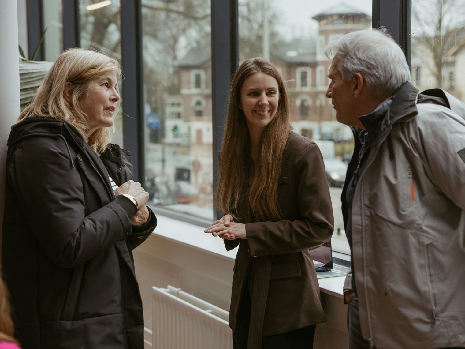 A TravelEssence specialist talks to two customers while smiling in front of a window