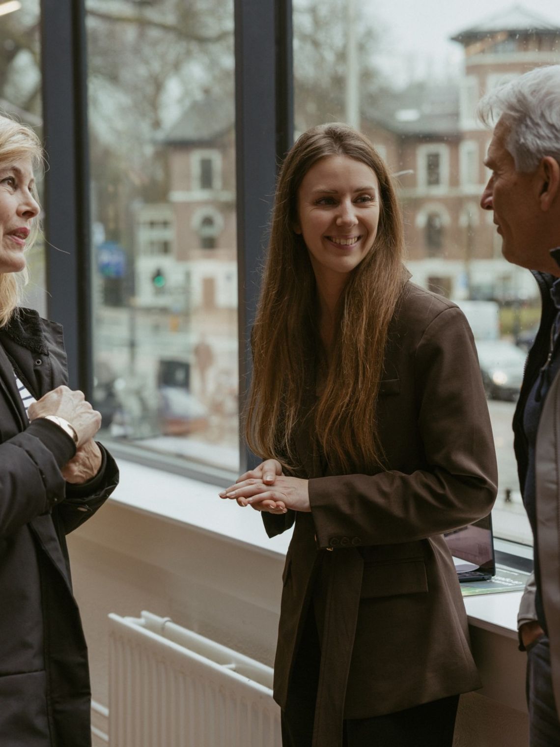 A TravelEssence specialist talks to two customers while smiling in front of a window