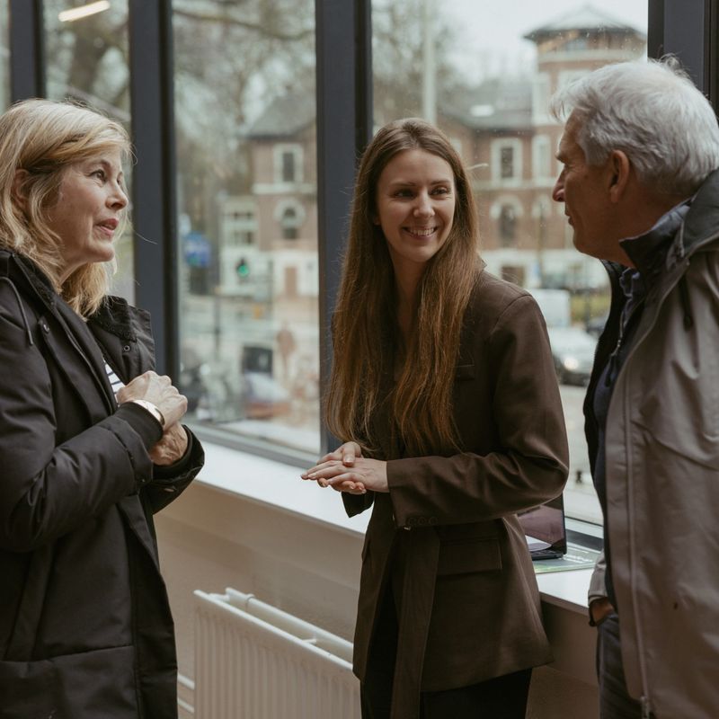 A TravelEssence specialist talks to two customers while smiling in front of a window