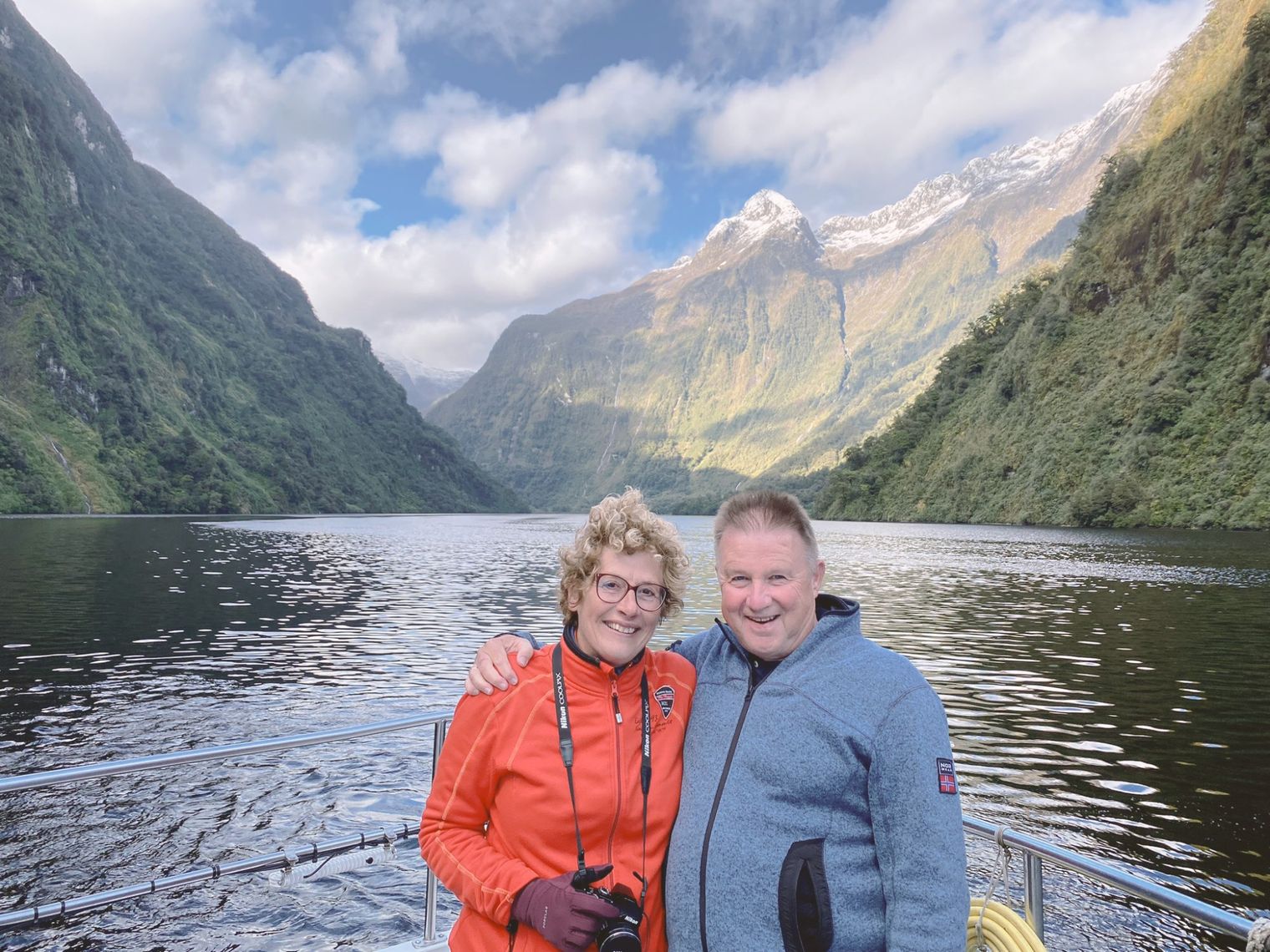 Een stel dat poseert op een boot, met achter hen de schilderachtige steile bergtoppen van het Fiordland National Park