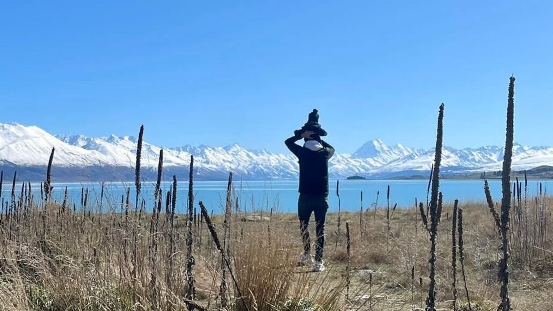 Elternteil mit Kind blickt über den Lake Tekapo zum Mount Cook, Neuseeland