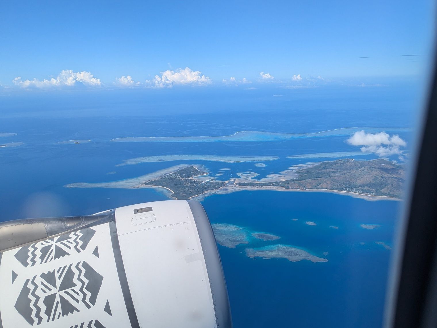 Uitzicht uit het raam van een vliegtuig van Fiji Airways dat over de eilanden van Fiji vliegt
