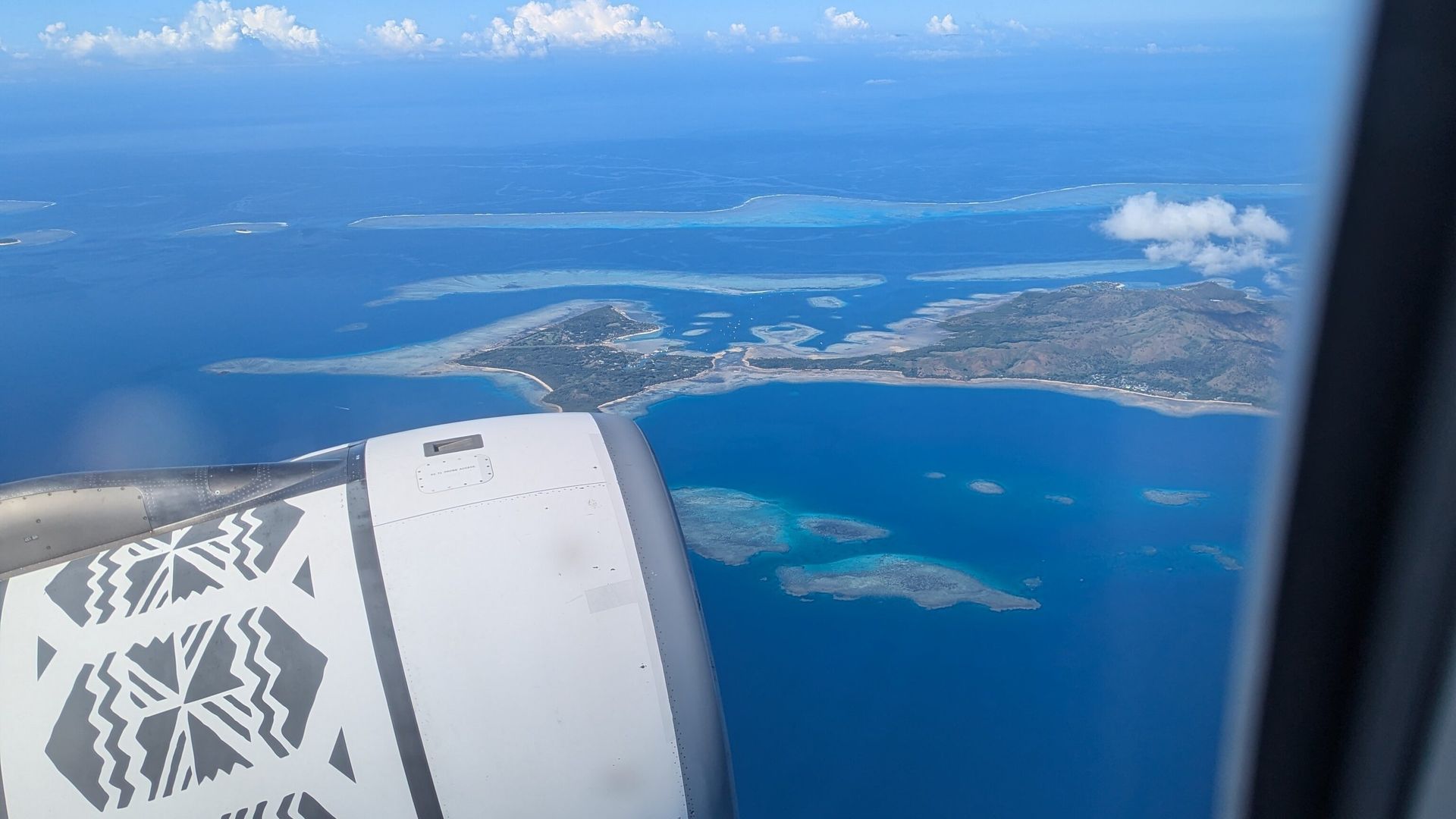 Uitzicht uit het raam van een vliegtuig van Fiji Airways dat over de eilanden van Fiji vliegt