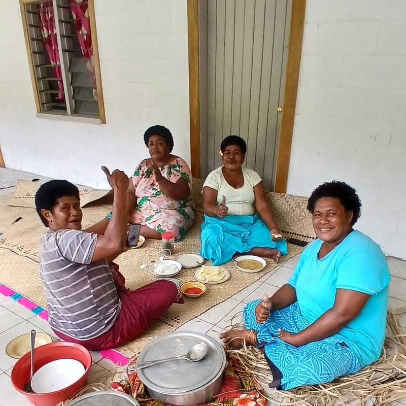 Een groep vrouwen zit op de grond en lacht naar de camera in het dorp Fiji
