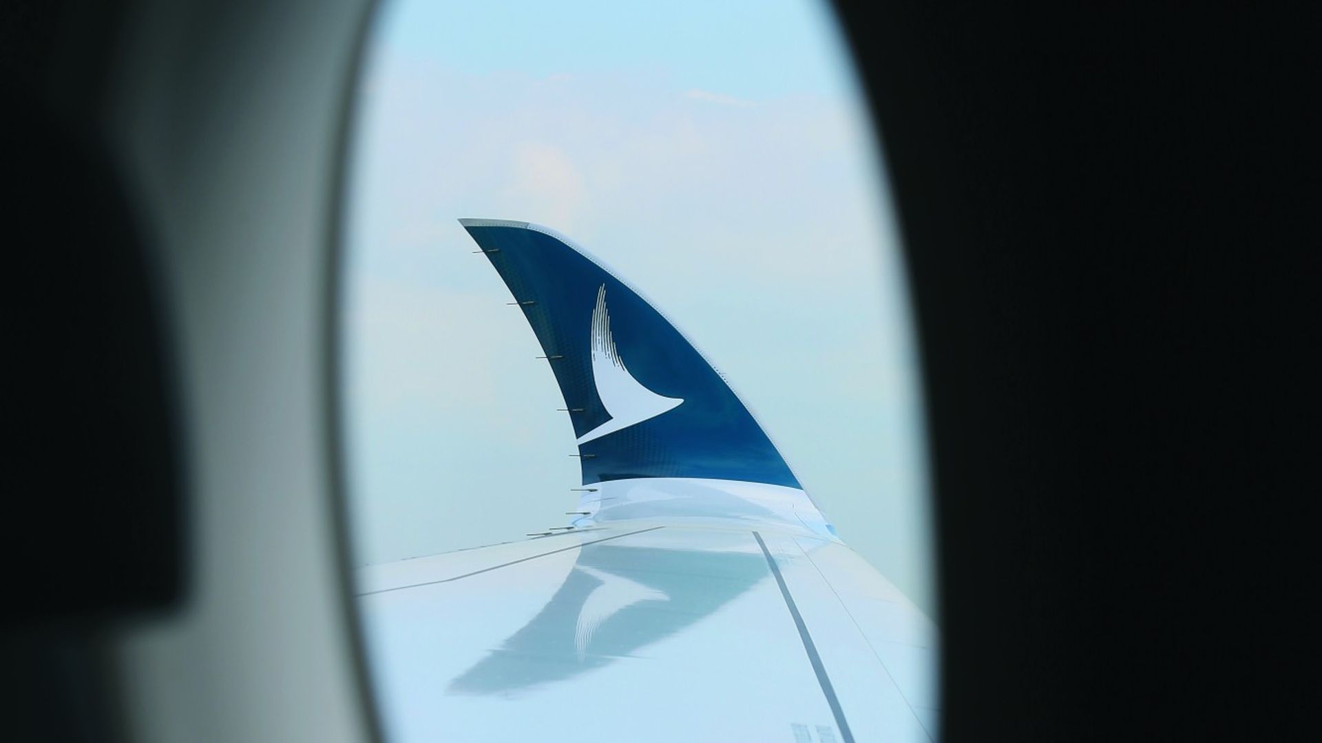 Aanzicht van een vliegtuigvleugel door het vliegtuigraampje. Op de vleugel is het logo van Cathay Pacific zichtbaar.