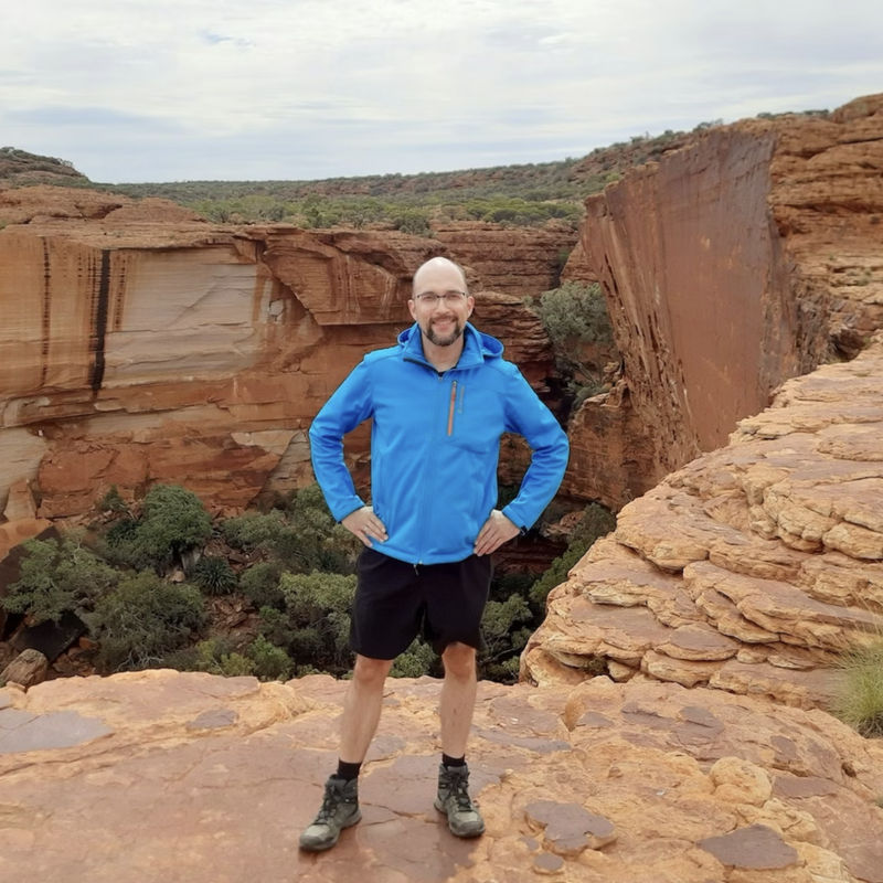 Mann mit blauer Jacke steht vor roter Felsenschlucht in Australien