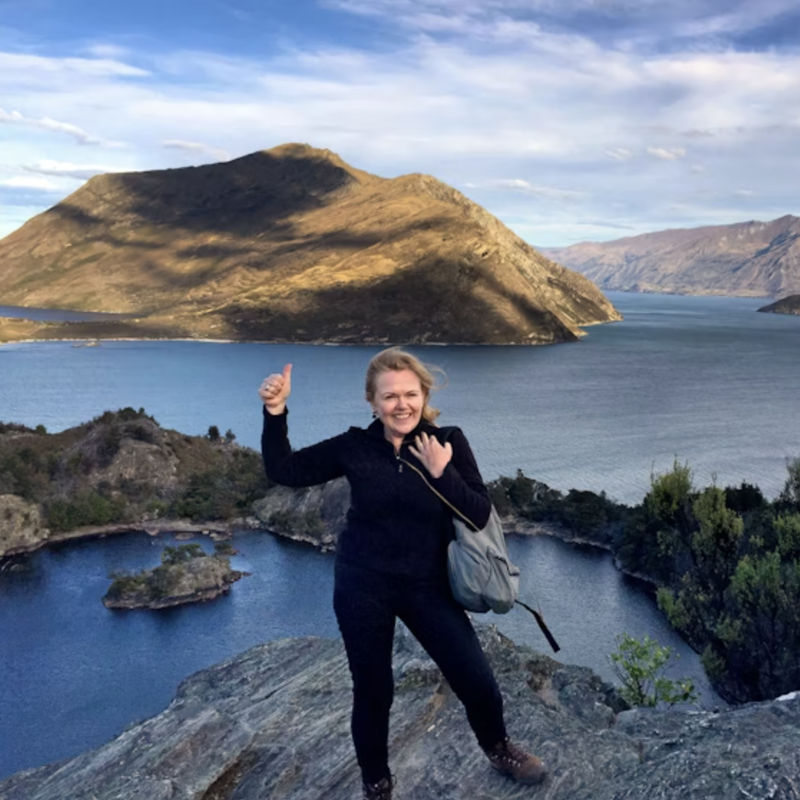 Vrouw glimlacht en geeft een duim omhoog naar de camera met de oceanen en bergen op de achtergrond
