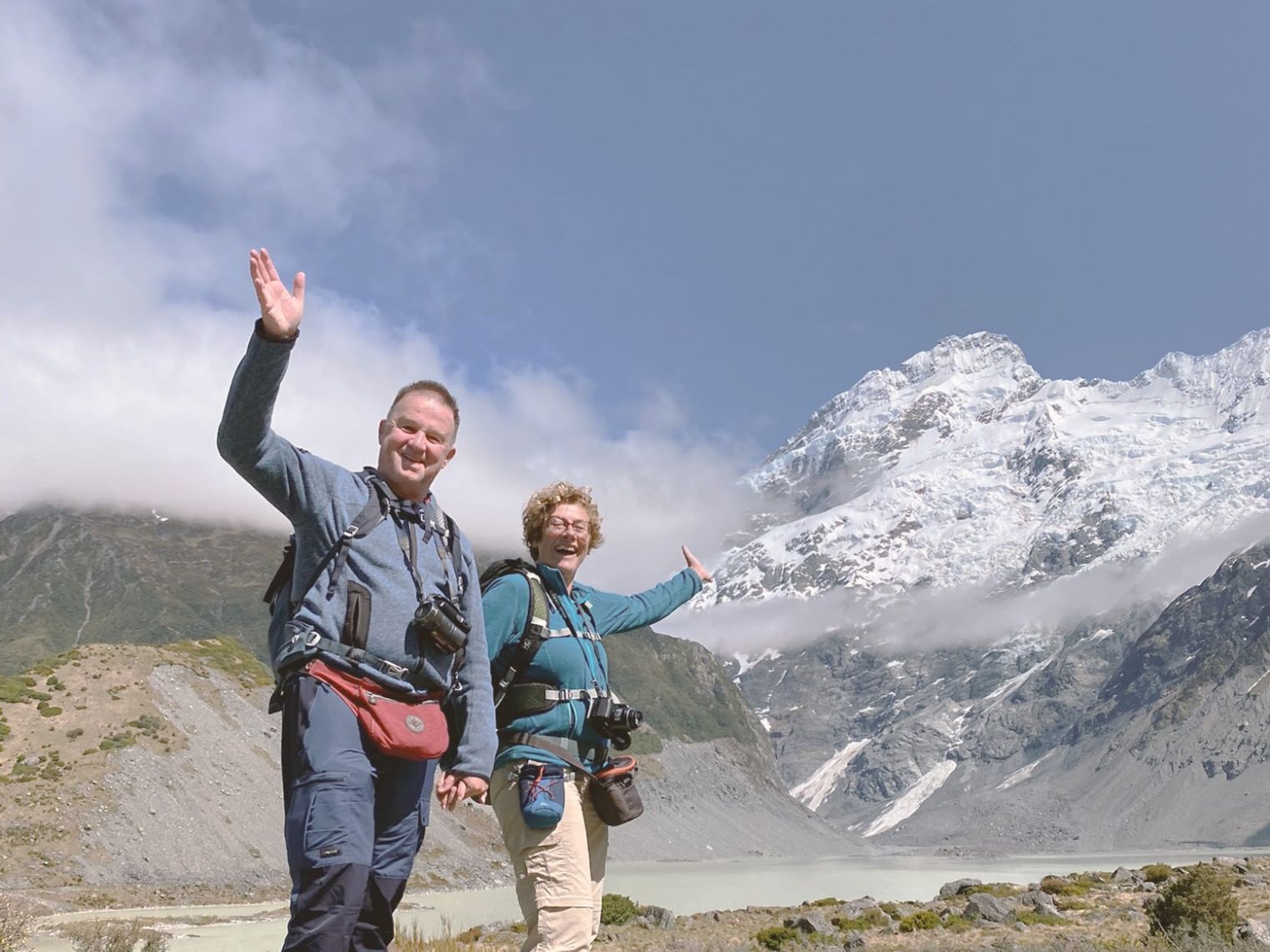Wandelaars poseren tegen de achtergrond van de met sneeuw bedekte Mount Cook, die hoog boven een gletsjerlandschap uittorent langs de Hooker Valley Track in Nieuw-Zeeland