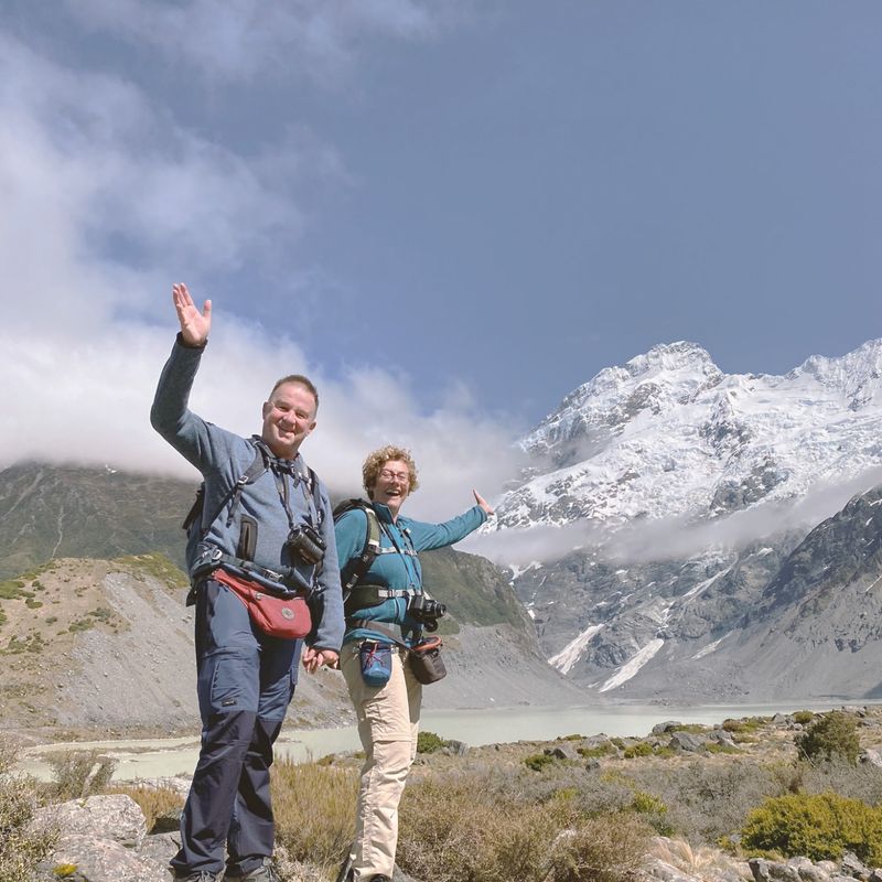 Wandelaars poseren tegen de achtergrond van de met sneeuw bedekte Mount Cook, die hoog boven een gletsjerlandschap uittorent langs de Hooker Valley Track in Nieuw-Zeeland