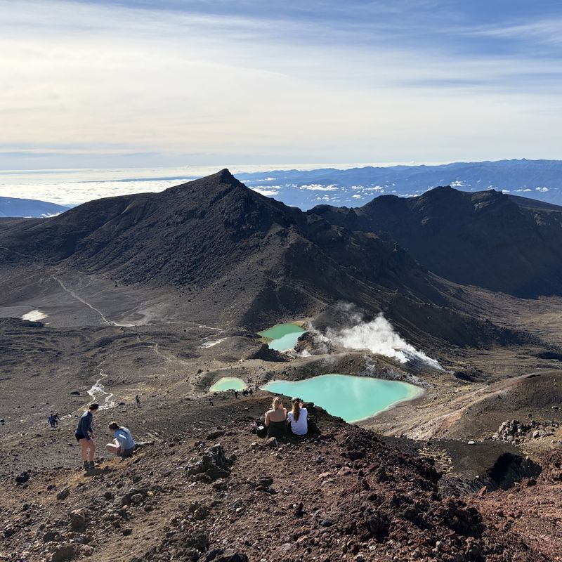 Wandelaars rusten boven de Emerald Lakes met rokende vulkanische openingen op de Tongariro Alpine Crossing, Nieuw-Zeeland