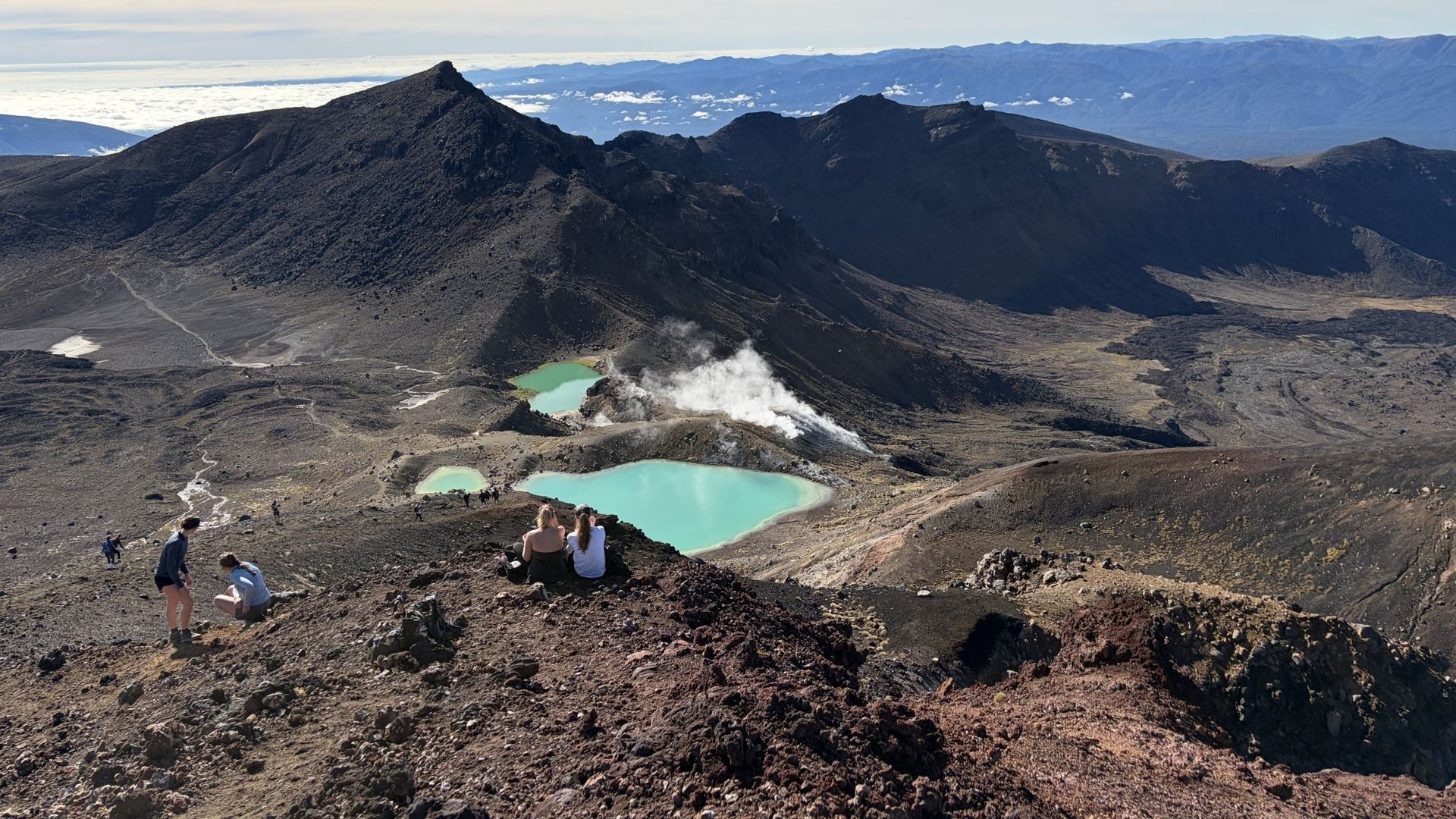 Wandelaars rusten boven de Emerald Lakes met rokende vulkanische openingen op de Tongariro Alpine Crossing, Nieuw-Zeeland