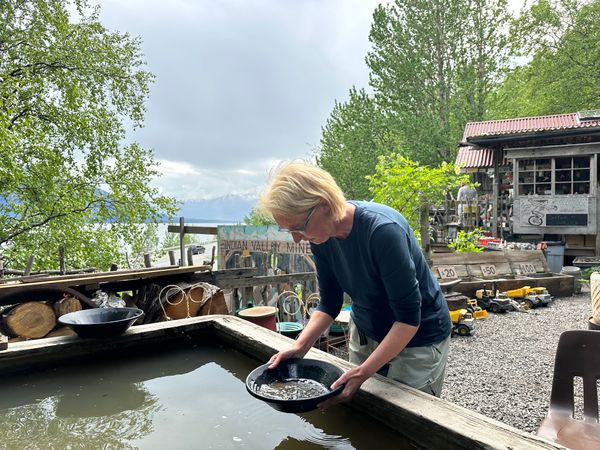 Vrouw die gebogen staat over water en in een schaaltje naar goud zoekt