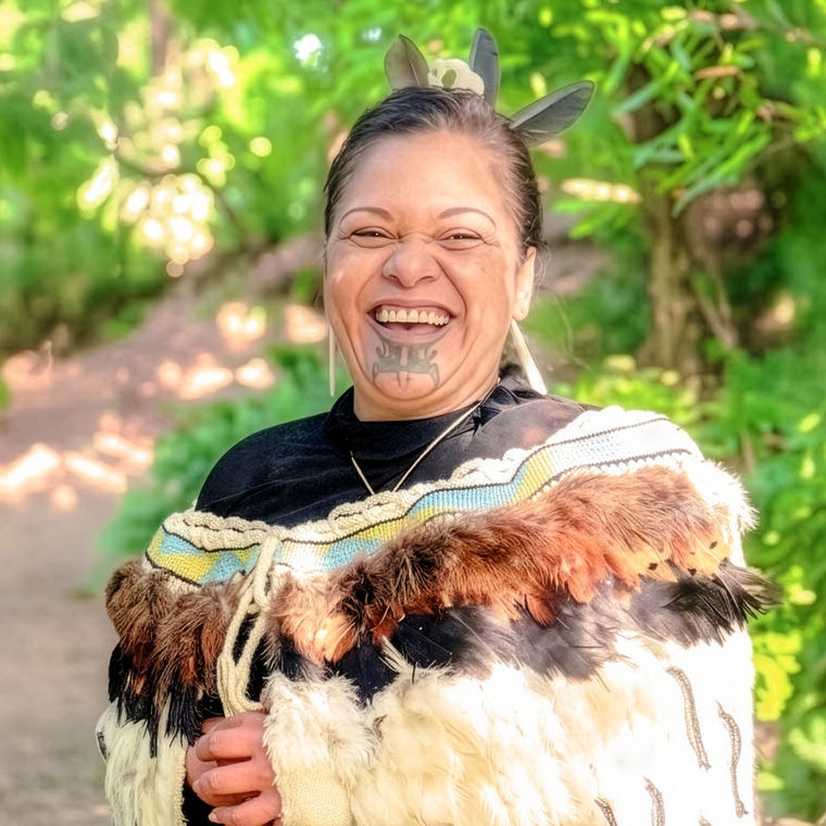 Die lächelnde Māori-Frau Maria, die einen traditionellen Federmantel und ein Tā-Moko-Gesichtstattoo trägt, heißt als einheimische Gastgeberin in Neuseeland Besucher willkommen