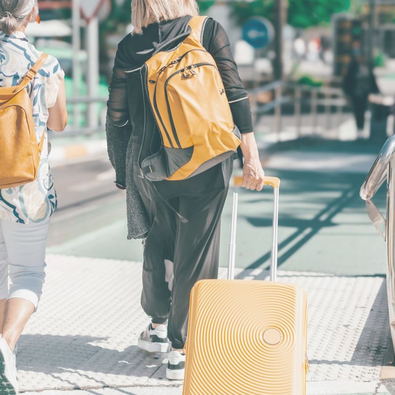 Two people walking to an airport wearing backpacks and one has a pull along suitcase