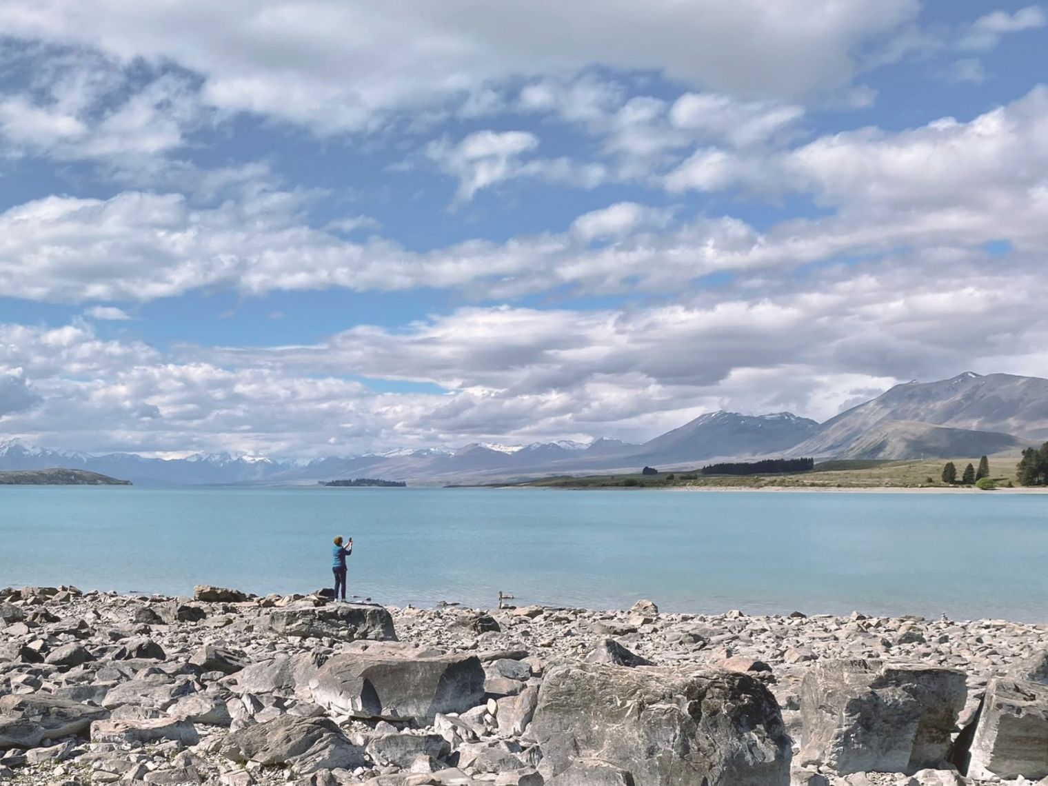 Een persoon die op de rotsachtige oever van Lake Pukaki staat, een adembenemend bergmeer op het Zuidereiland van Nieuw-Zeeland