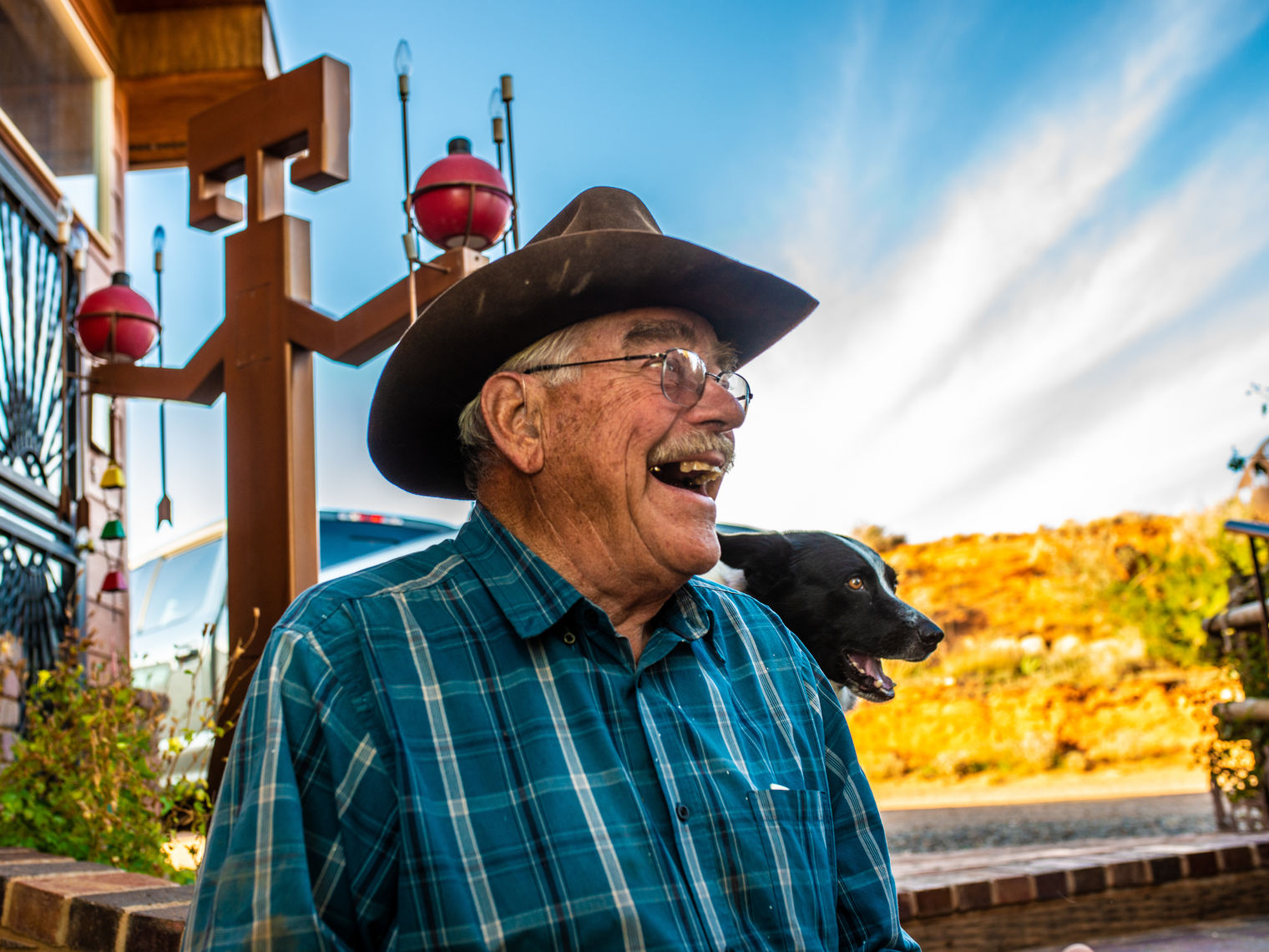 Der pensionierte Cowboy und Besitzer einer Gäste-Ranch Jerry Kinknade schaut nach rechts von der Kamera und lächelt, sein Hund und seine Ranch sind hinter ihm zu sehen.