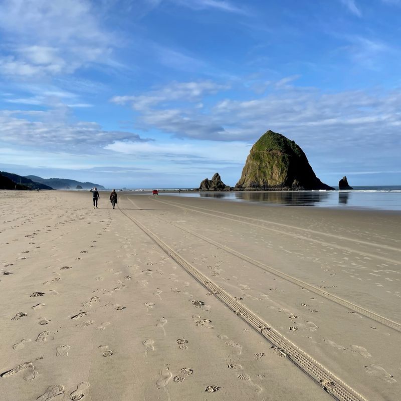 Twee mensen lopen over het strand van Cannon Beach richting een grote rotsformatie die uit de zee oprijst.