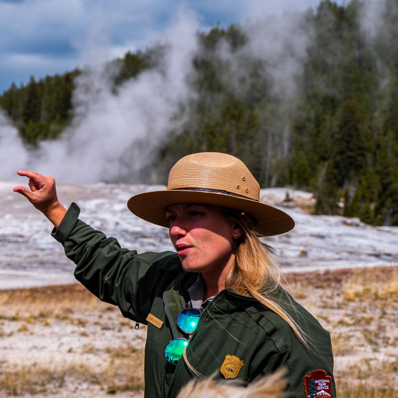 A Yellowstone park ranger gives an explanation to visitors about a geyser in the background